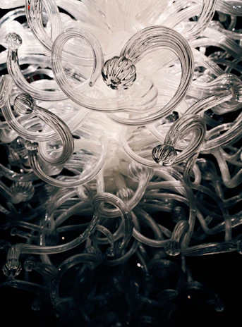 A sculptural installation featuring intertwined metal and glass elements reflecting soft gallery lighting.