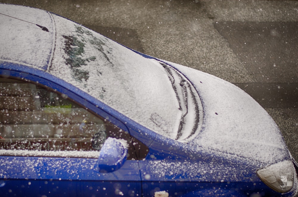 a blue car covered in snow on a city street