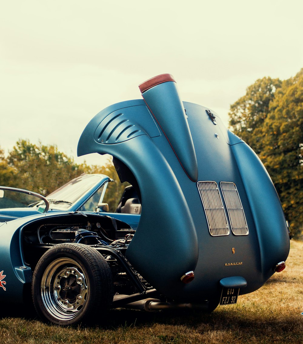 a blue car with its hood open sitting in the grass