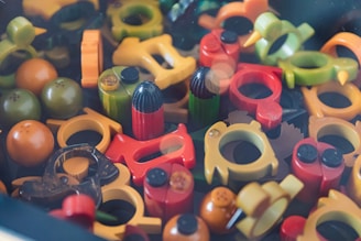A collection of various colorful plastic objects, including rings, round shapes, and small figurines. The objects are scattered randomly, creating a dense and chaotic arrangement with an assortment of shapes and colors. Some items appear to have small black caps on them.