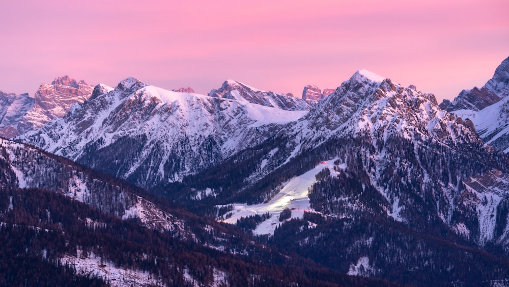 a mountain range covered in snow with a pink sky