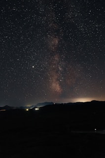 A night sky panorama featuring the Milky Way stretching across a clear, star-filled sky.