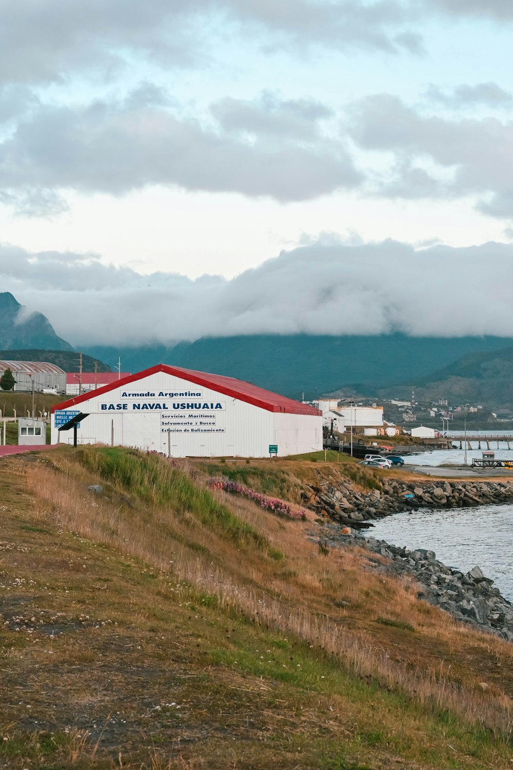 a red and white building sitting on top of a hill next to a body of