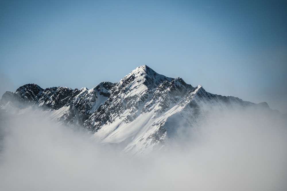 a snow covered mountain in the middle of a cloud filled sky