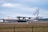 A large cargo airplane is taxiing on a runway at an airport. The aircraft is white with blue and yellow accents and has the word 'ANTONOV' displayed prominently on its tail fin. The background features a cloudy sky and some distant airport infrastructure.
