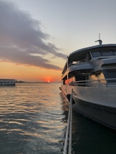 A sleek boat docked at sunset with calm waters reflecting the orange sky.