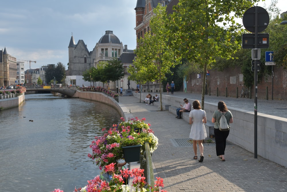 a couple of women walking down a sidewalk next to a river