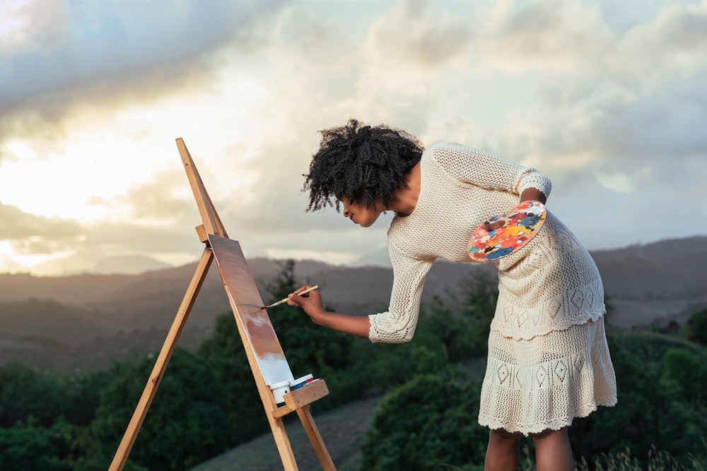 a woman is painting on an easel in a field