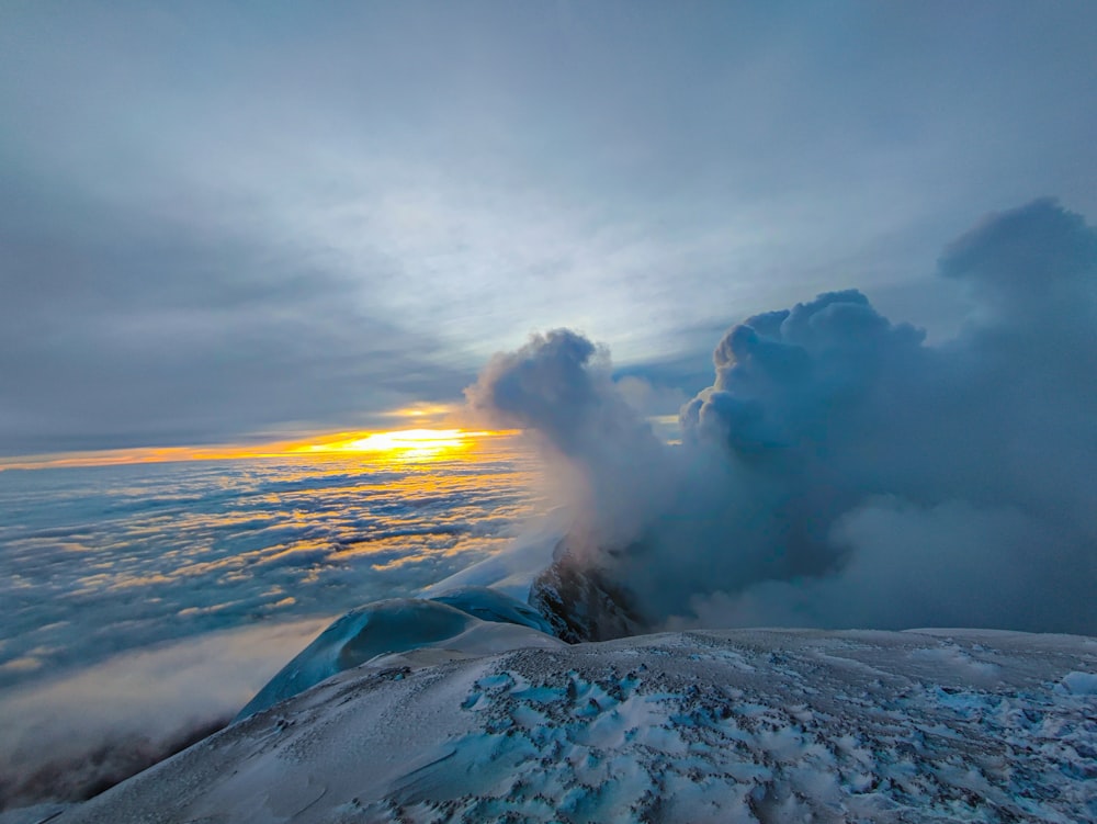 the sun is setting over the clouds above a mountain