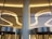 A modern architectural interior featuring sleek, curved ceiling lights and large glass panels. The lighting is warm, creating elegant reflections on the metallic surfaces of the revolving doors below.