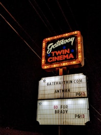 A classic cinema marquee sign illuminated against the night sky. The upper section features the text 'Gateway Twin Cinema' bordered with chasing lights, while the lower section lists movie titles such as 'Antman' and '80 for Brady', both rated PG13.