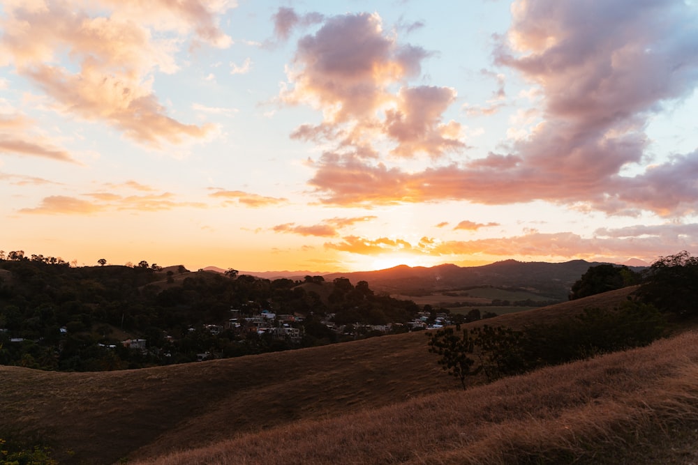 the sun is setting over a hilly area