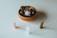 A collection of polished stones and crystals is arranged, featuring a small bowl filled with smooth, rounded dark and light stones, accompanied by three upright crystal points in pink, clear, and brown colors on a white surface.