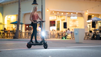 A happy customer riding an evox scooter through a city street at dusk, purple gradient sky overhead.
