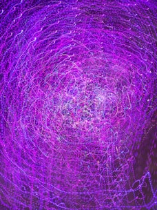 A swirling pattern of vibrant purple and hints of blue light trails creates a dynamic and abstract visual effect. The image resembles a vortex or tunnel of light, filled with intricate details and motion.