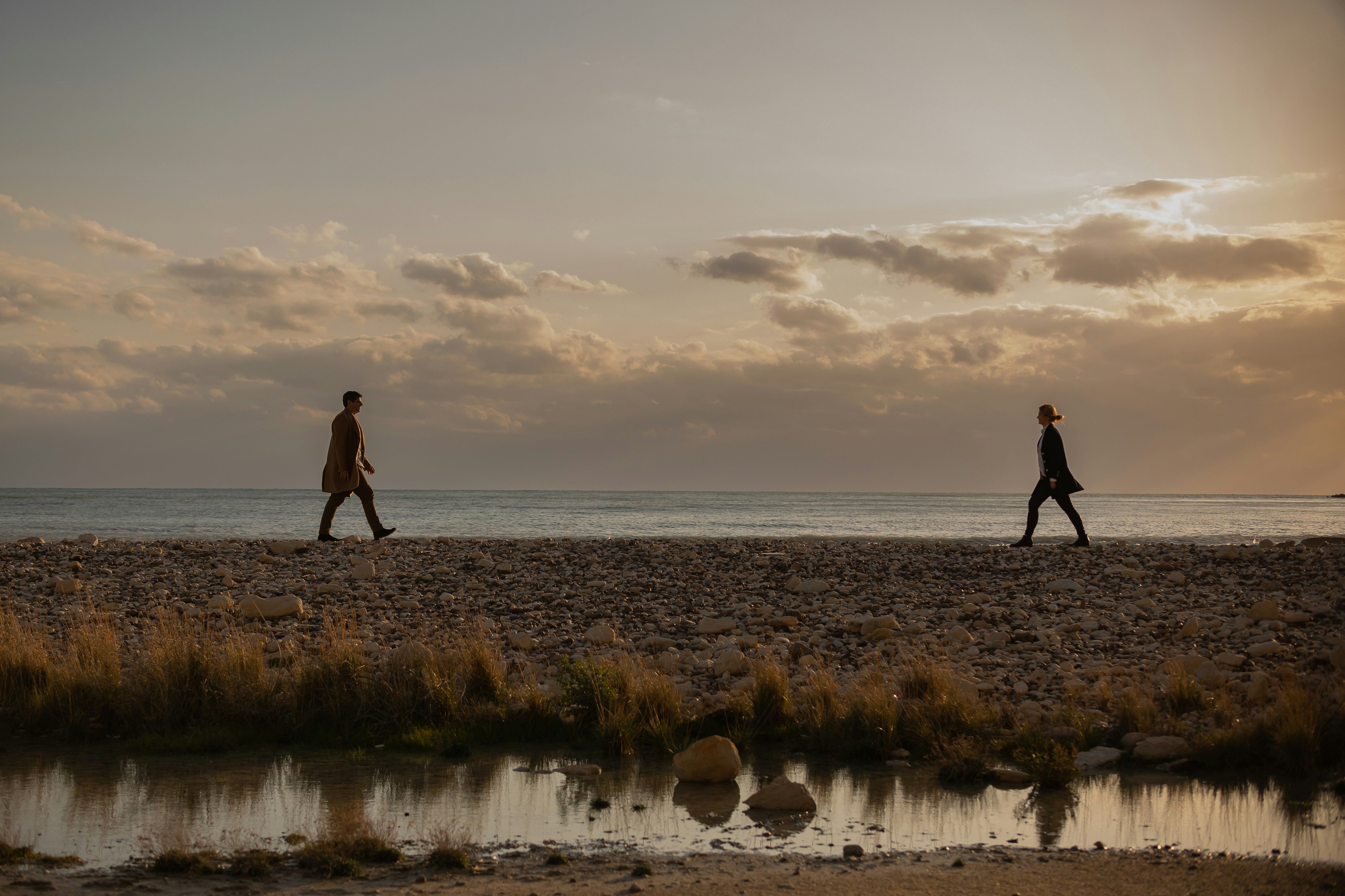 a couple of people walking across a sandy beach