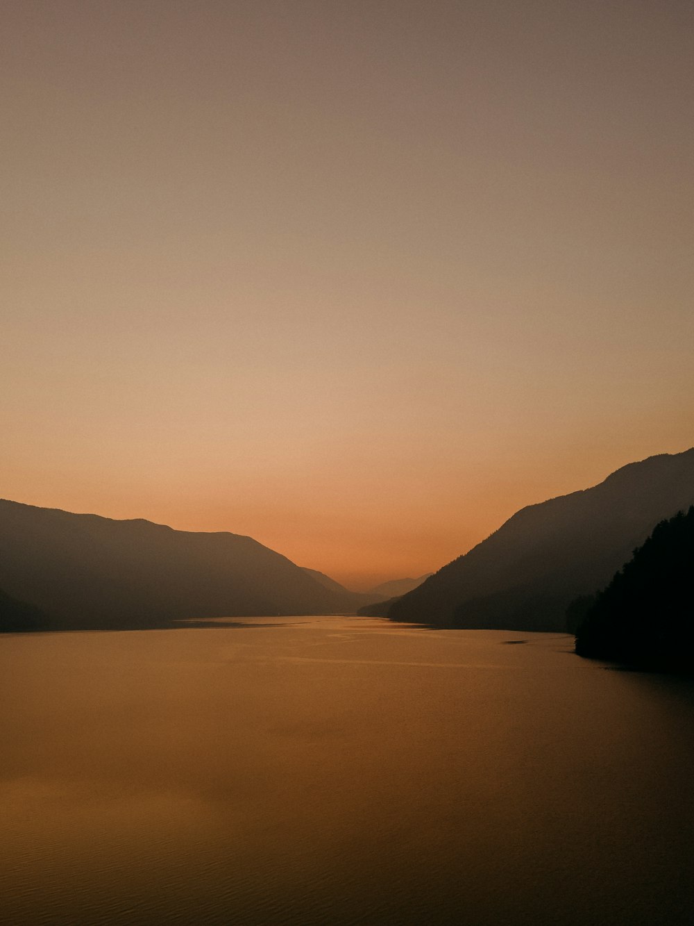 the sun is setting over a lake with mountains in the background