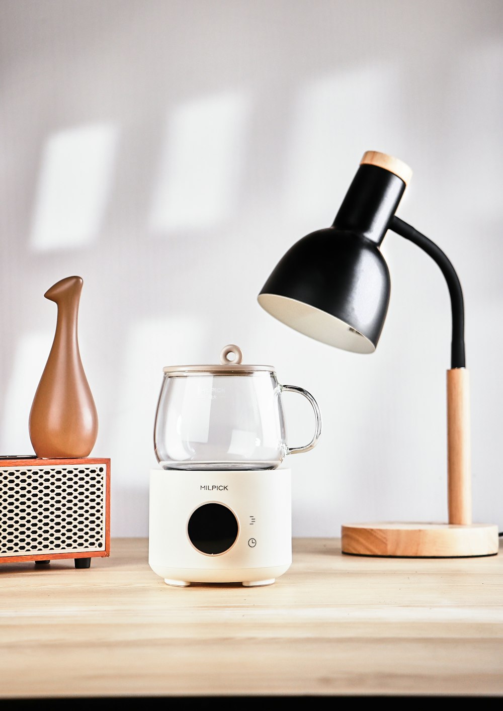 a table with a lamp, a coffee pot, and a speaker on it