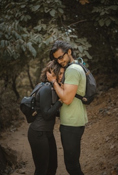 A candid moment of the couple hiking with their dogs on a forest trail surrounded by soft green foliage.