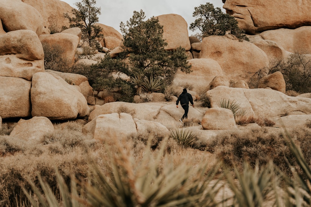 a man in a black suit walking through a rocky area
