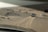 A desert landscape with sand dunes featuring two off-road vehicles driving on the tracks. Sparse vegetation is scattered across the sandy terrain, and tire tracks are visible behind the vehicles.