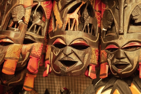 A collection of intricately carved wooden masks with detailed patterns and designs. Each mask features animal motifs such as giraffes and other wildlife, surrounded by bright colors and traditional African art styles.