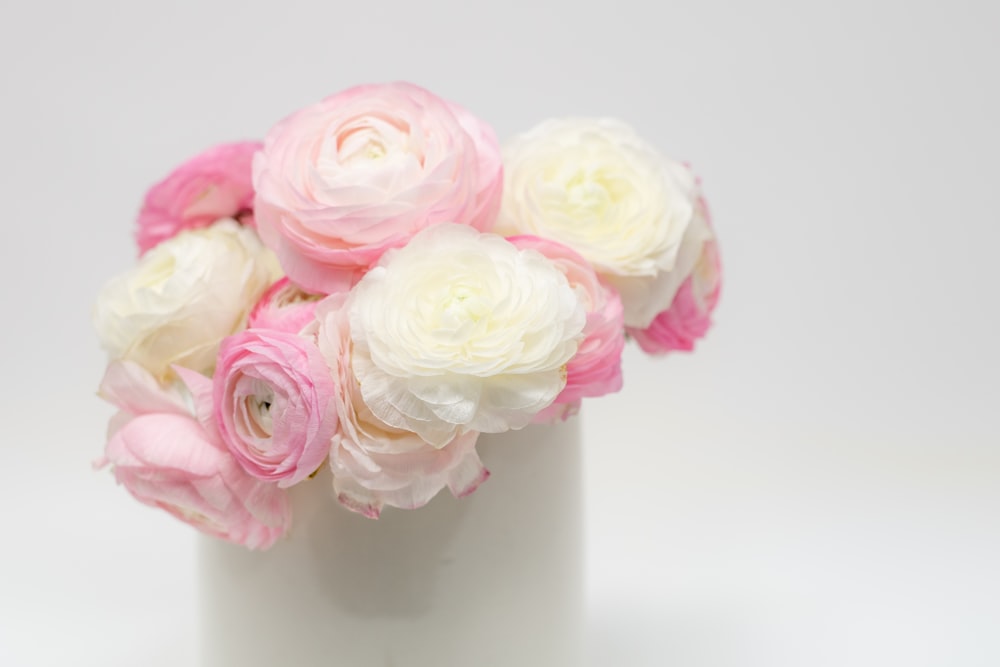 Un jarrón blanco lleno de flores rosadas y blancas