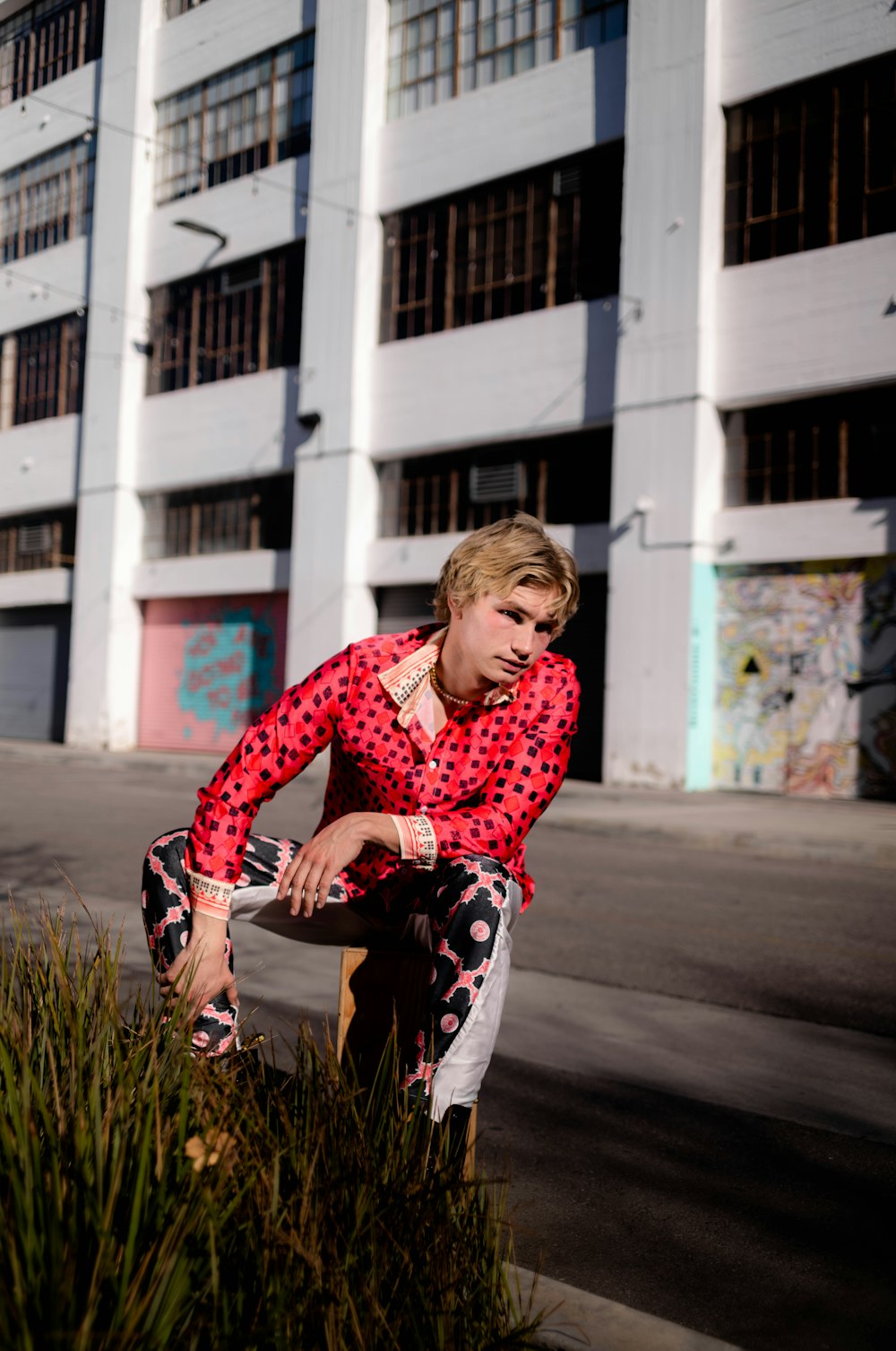 a man in a red and black shirt leaning on a plant