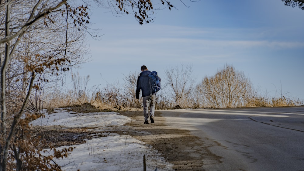 a man with a backpack walks down a snowy road