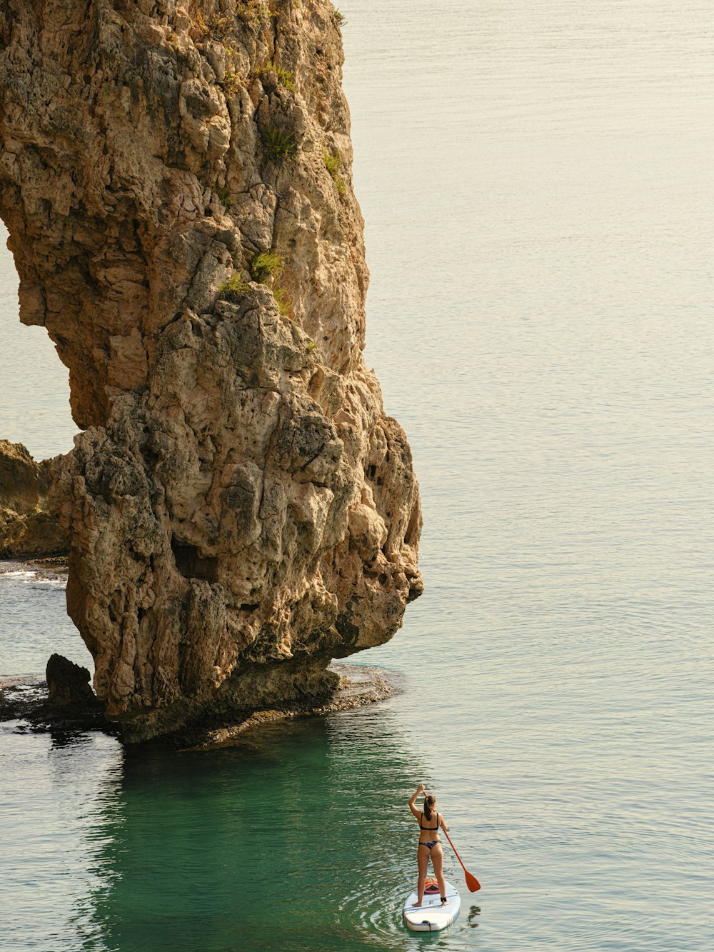 a person on a surfboard in the water near a large rock