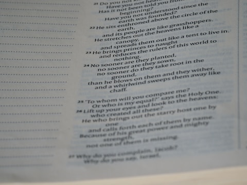 A page from a book containing biblical text with numbered verses. The right side of the page features text in a two-column format, while the left side shows faint dotted lines without text. The background is an off-white color with the text primarily in black, and there is a slight shadow over parts of the page.