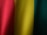 Vertical folds of fabric display a gradient of colors ranging from red to yellow to green. The texture of the fabric is visible, showing a fine weave pattern.