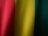 Vertical folds of fabric display a gradient of colors ranging from red to yellow to green. The texture of the fabric is visible, showing a fine weave pattern.