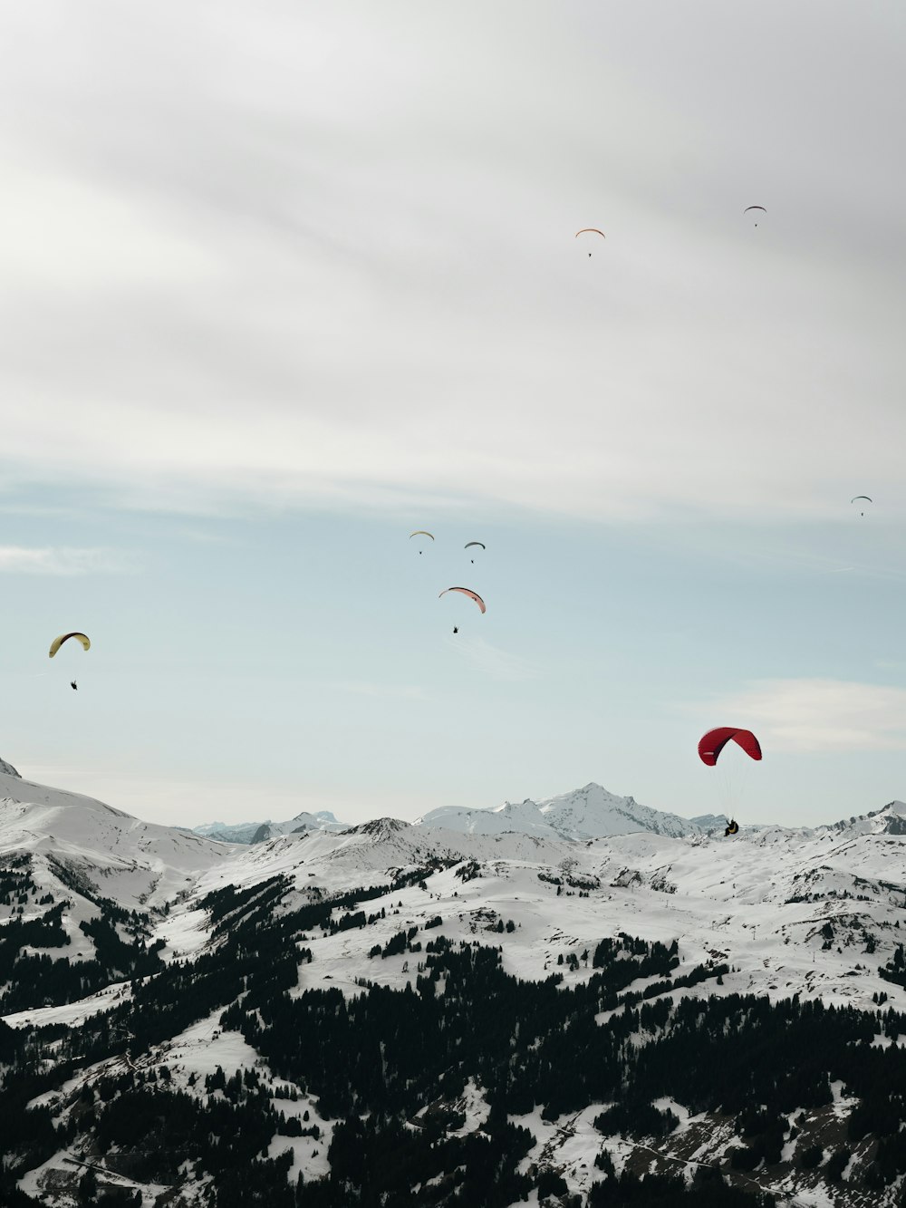 a group of people flying kites over a snow covered mountain