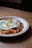 A plate of kimchi fried rice topped with a sunny-side-up egg, garnished with chopped green onions, is placed on a wooden table.