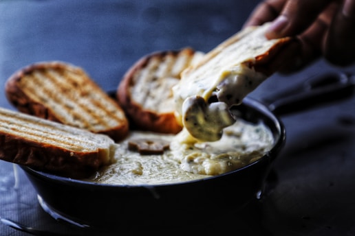 Close-up of a bubbling cheese fondue pot surrounded by fresh bread and charcuterie.
