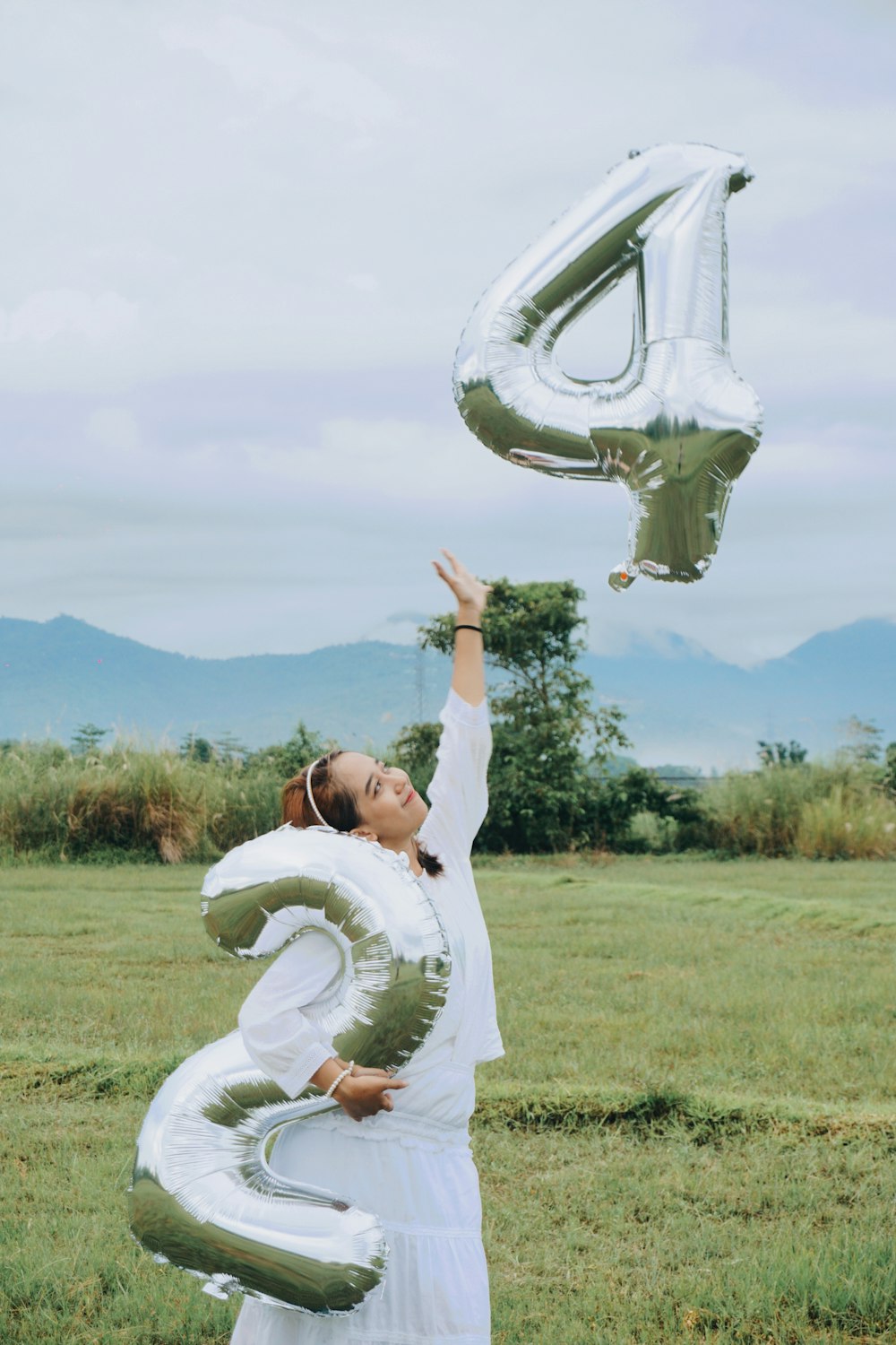 a woman in a white dress holding up a number six balloon