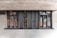 A neatly organized drawer contains various cutlery and kitchen utensils. On the left side, there are compartments filled with bronze-colored spoons, forks, and knives. The center section holds multiple brass napkin rings. On the right side, there are stainless steel spoons and forks, as well as knives with wooden handles. The drawer is set in a wooden cabinet under a marble countertop.