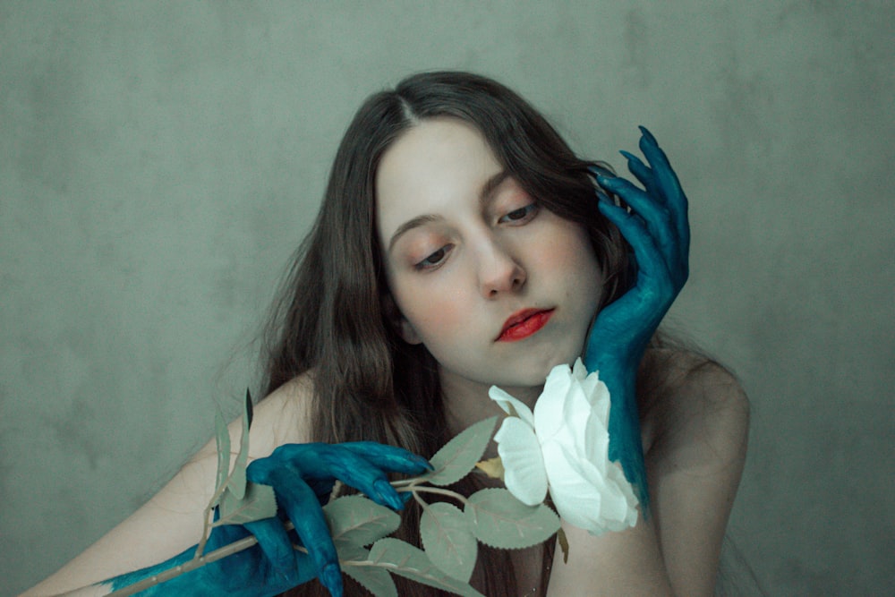 a woman with long hair and blue gloves holding a flower