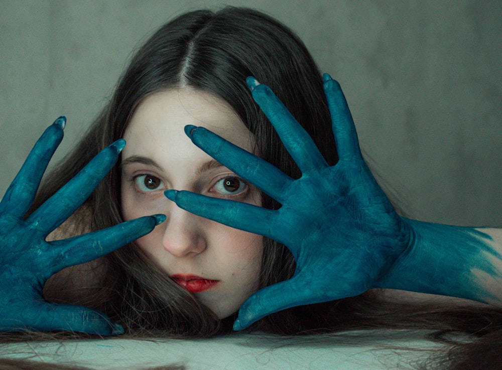a woman with blue painted hands covering her face