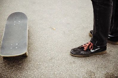 Casual rubber shoes resting beside a skateboard on pavement.