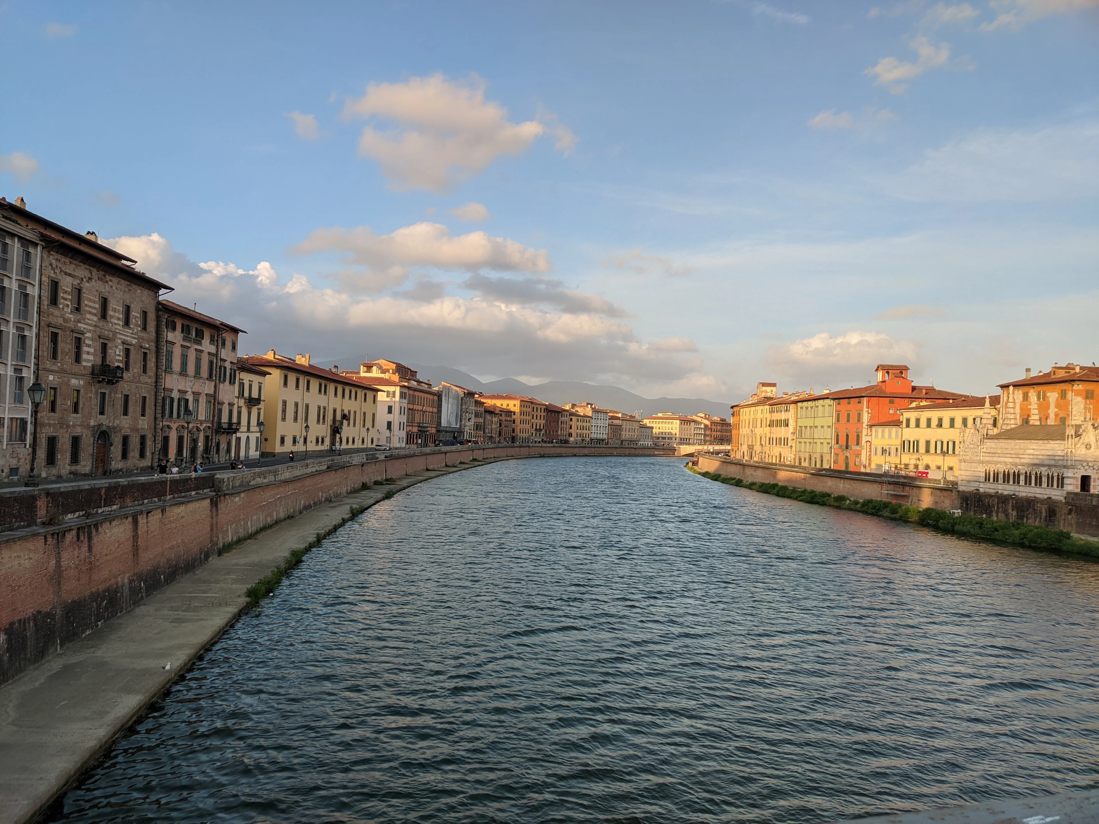 The Arno river glows at golden hour, historic buildings lining both banks of Pisa.