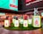 A colorful display featuring cartoonish animal figurines and signs with English and Chinese characters representing different animals of the Chinese zodiac, such as the rat, ox, and rabbit. The figures are placed on illuminated pedestals surrounded by artificial grass, set against the backdrop of a well-lit urban environment with restaurant signage in the background.