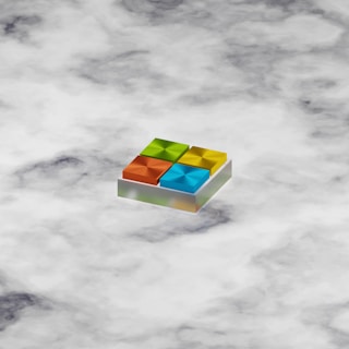 A 3D geometric shape resembling a logo with four colorful squares, each in a different color: orange, green, blue, and yellow. The squares are arranged in a grid on a slightly tilted platform, giving a sense of depth. The background consists of a cloudy pattern in various shades of white and gray.