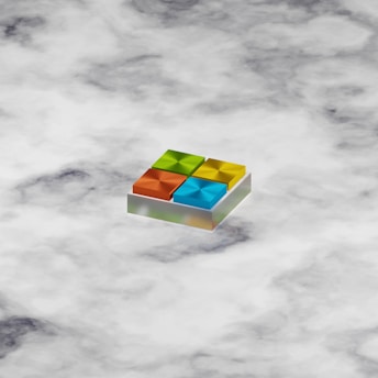 A 3D geometric shape resembling a logo with four colorful squares, each in a different color: orange, green, blue, and yellow. The squares are arranged in a grid on a slightly tilted platform, giving a sense of depth. The background consists of a cloudy pattern in various shades of white and gray.