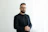 a man with a beard and glasses standing in front of a white wall