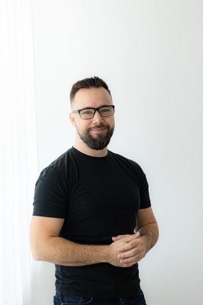 a man with a beard and glasses standing in front of a white wall