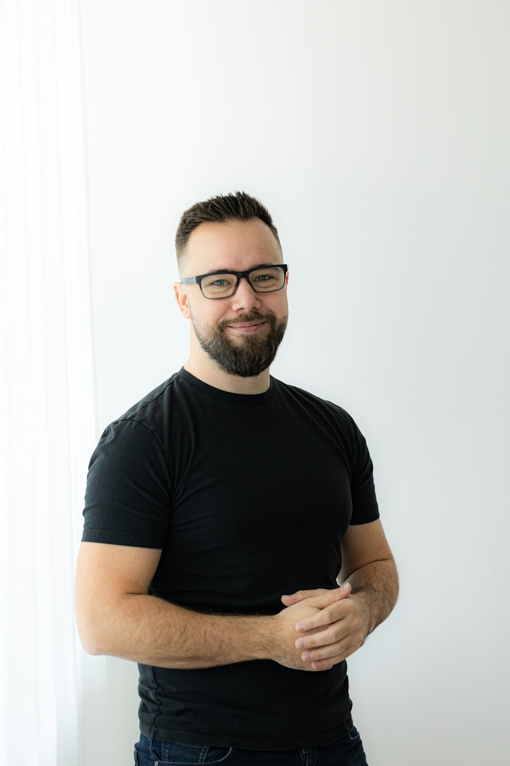 Un homme avec une barbe et des lunettes debout devant un mur blanc