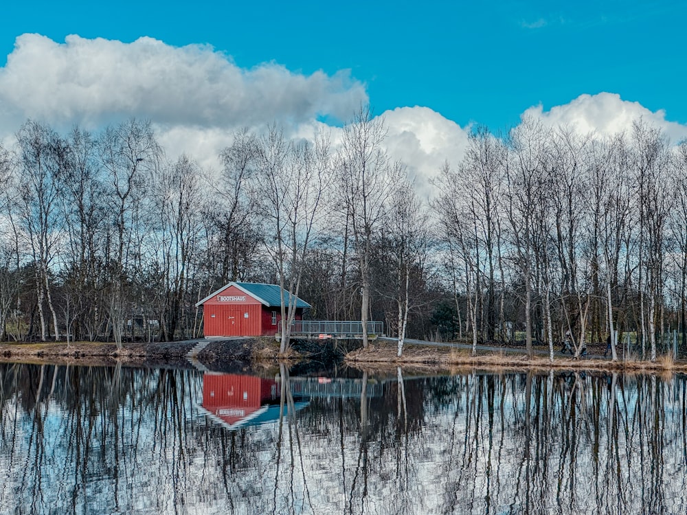 a red house sitting on top of a lake next to a forest