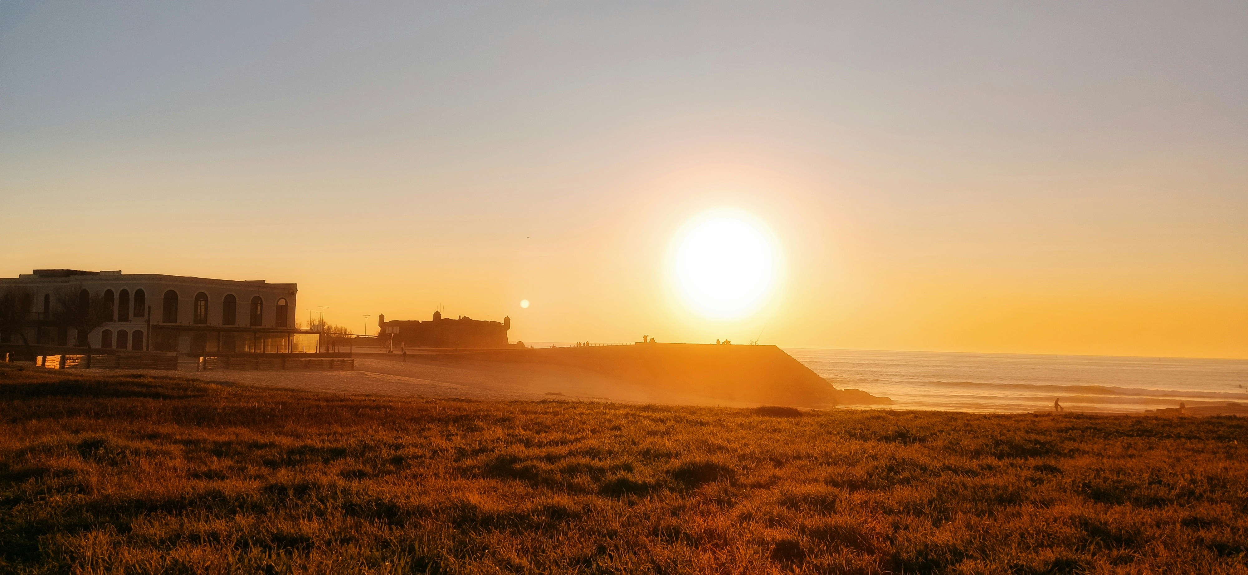 the sun is setting over a beach with a building in the background